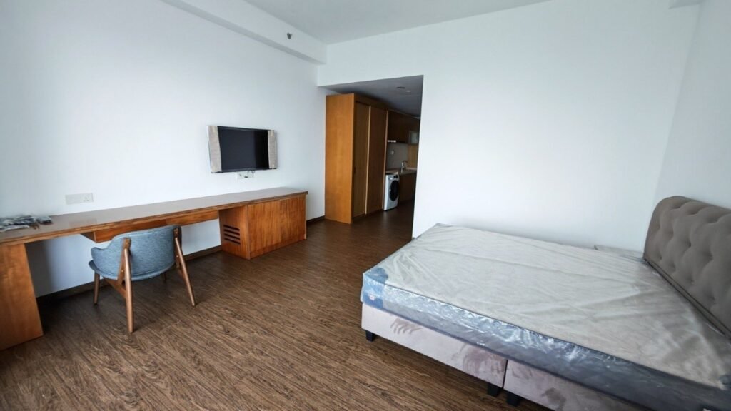 Studio interior with bed, desk, wall-mounted TV and open kitchen area.