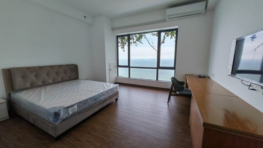 Bed positioned beside a large window overlooking the sea.