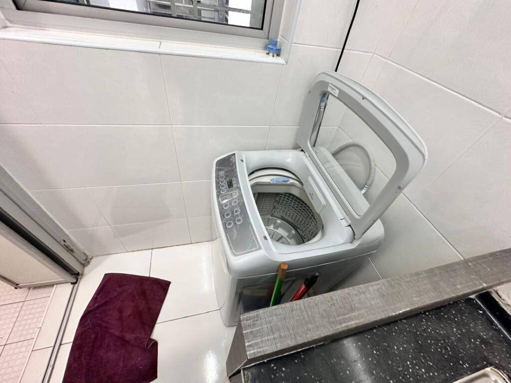 Laundry area with washing machine beside a tiled wall and window.