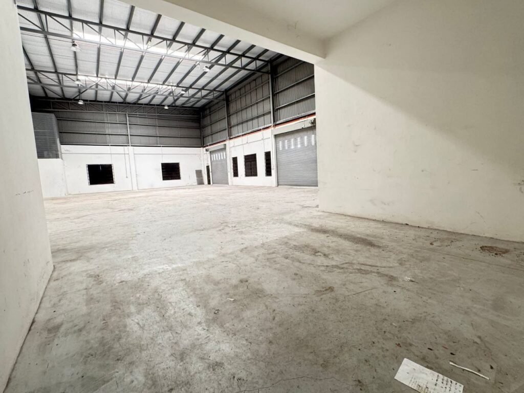 Wide interior view of a vacant industrial factory hall with high ceiling and roller shutters