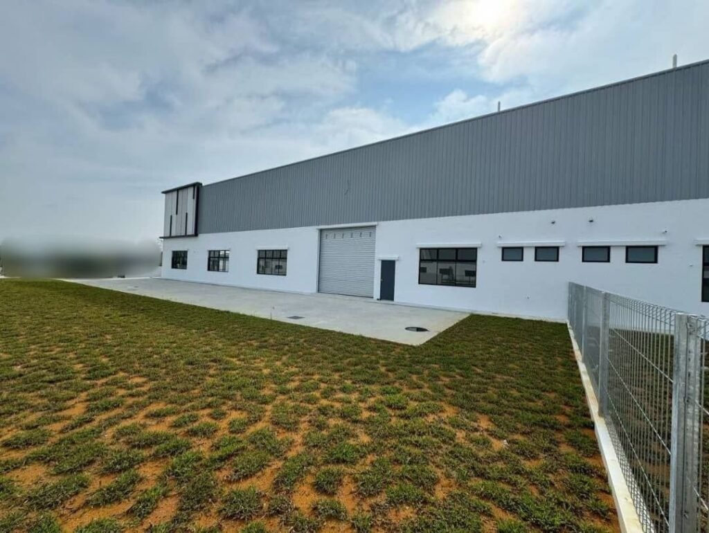 Exterior view of a single-storey industrial building with yard and fenced edge.